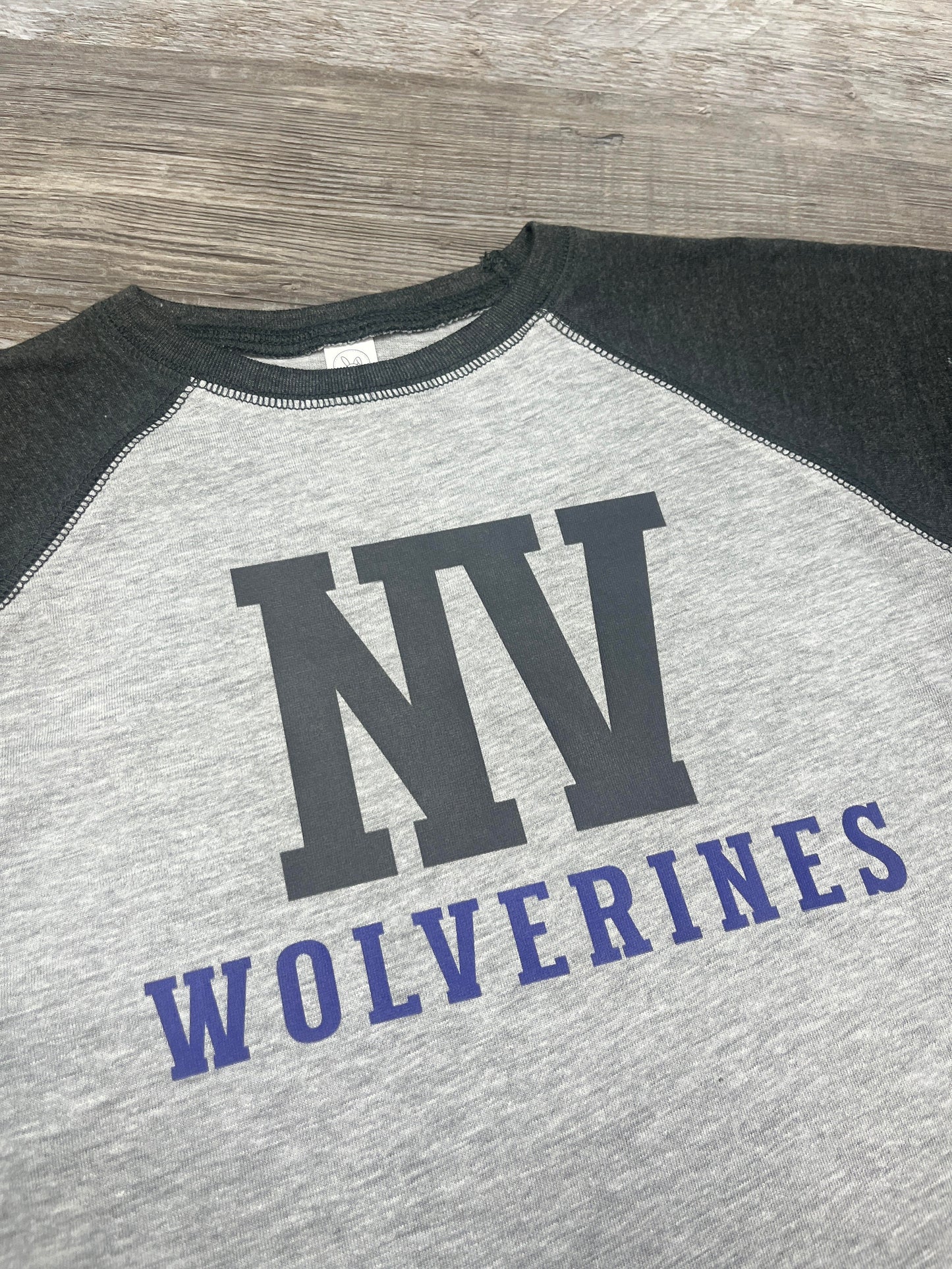 Gray and black baseball shirt with 'NV Wolverines' text on a wooden surface