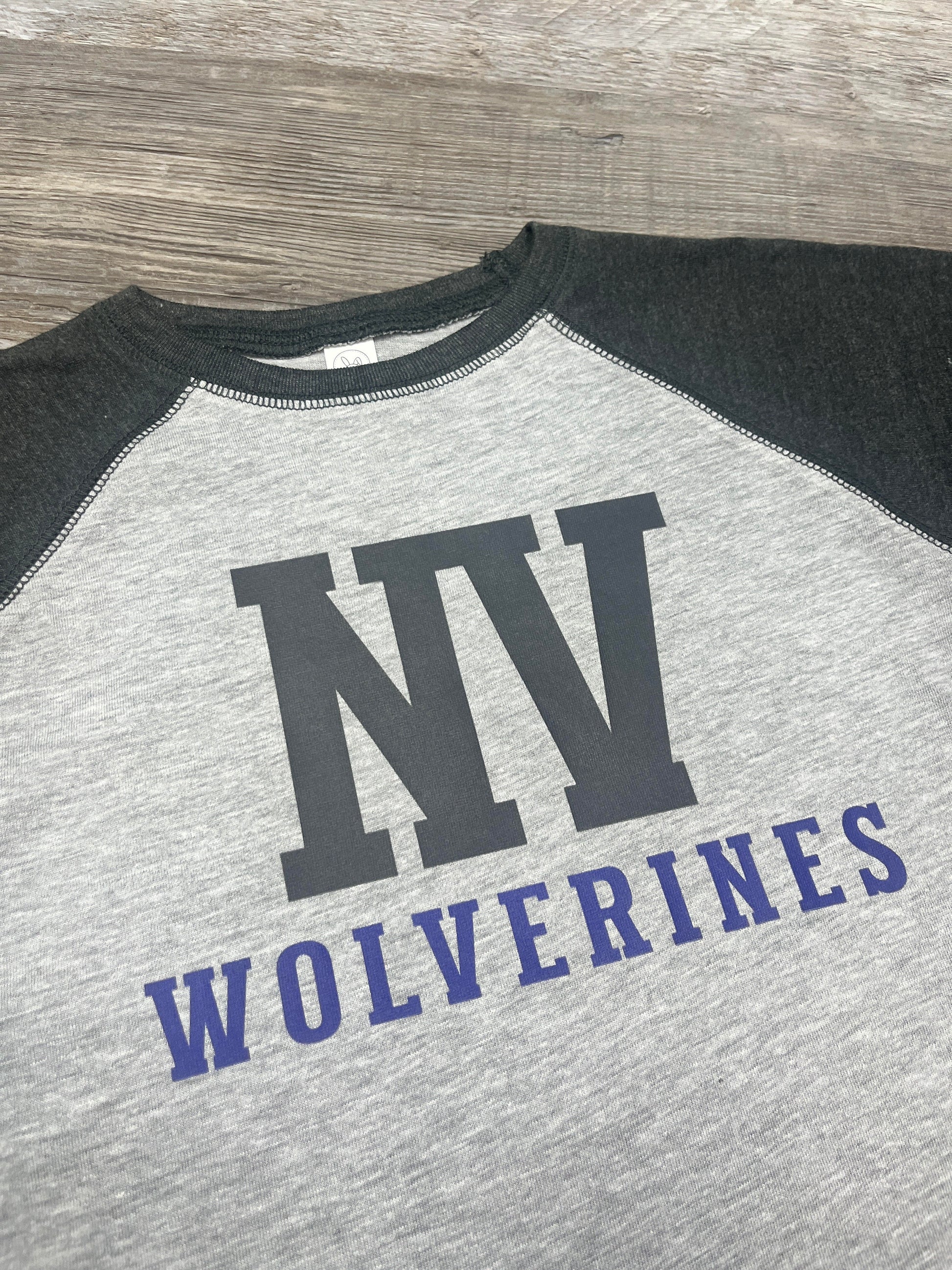 Gray and black baseball shirt with 'NV Wolverines' text on a wooden surface